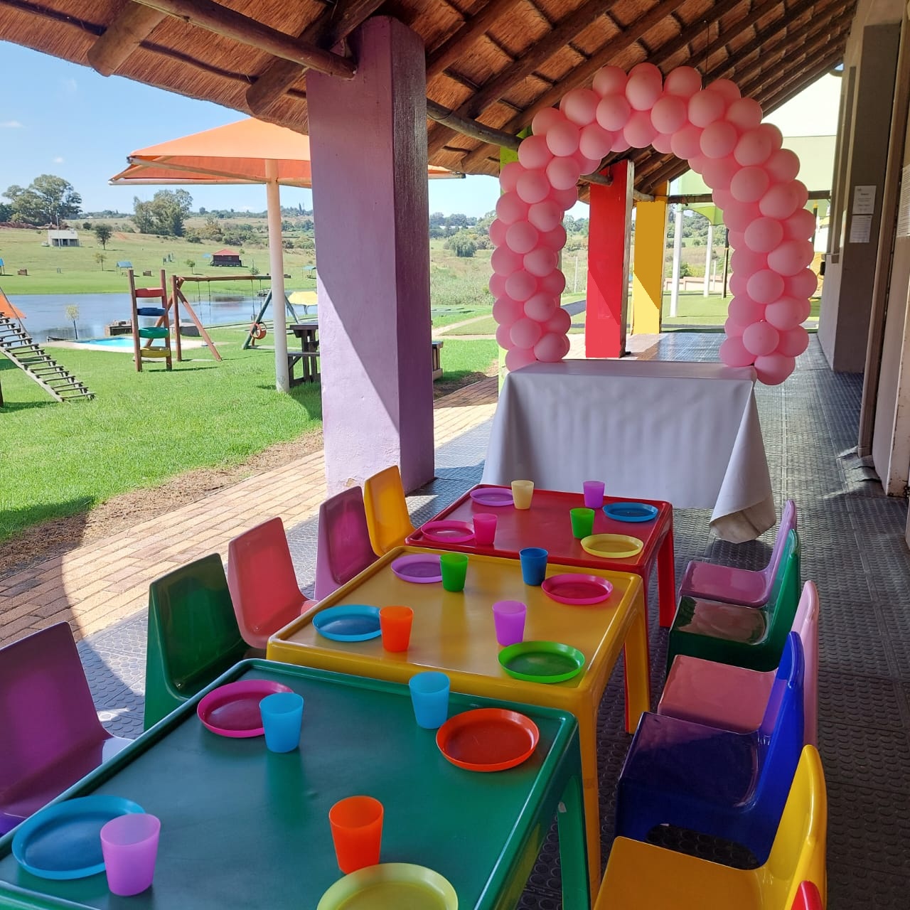 Thatched party lapa at Gnu Kids decorated with a pink balloon arch and colourful kids' party tables