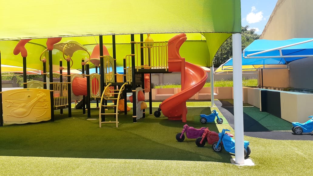 Outdoor shaded playground with red slide and ride-on bikes